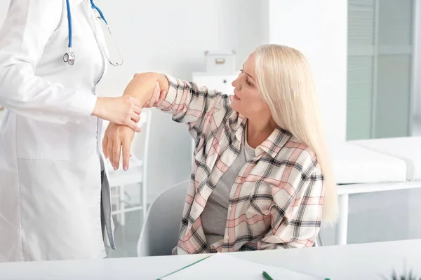 Врач осматривает зрелую женщину с болью в суставах в клинике — стоковое фото