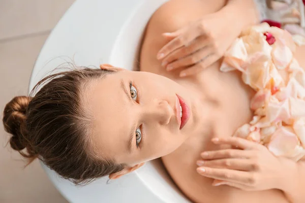 Bella giovane donna che fa il bagno con petali di fiori a casa — Foto Stock