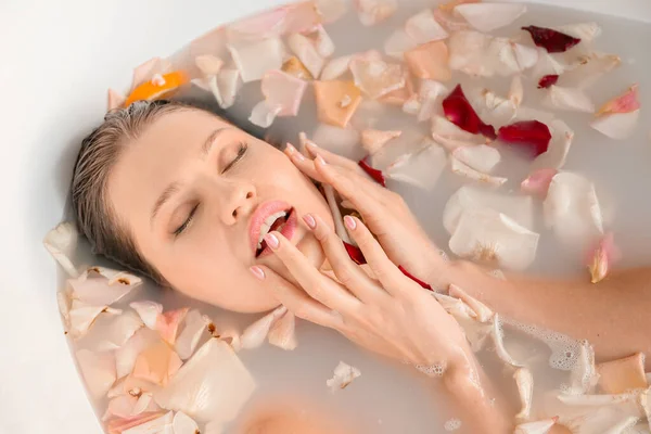 Schöne junge Frau badet zu Hause mit Blütenblättern — Stockfoto