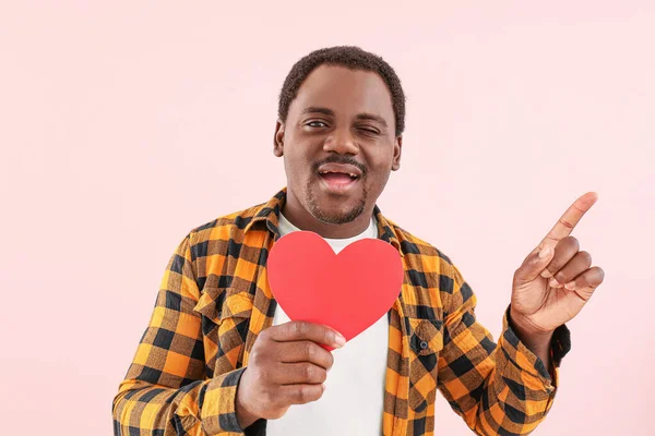 African-American man with red heart pointing at something on color background — Stock Photo, Image