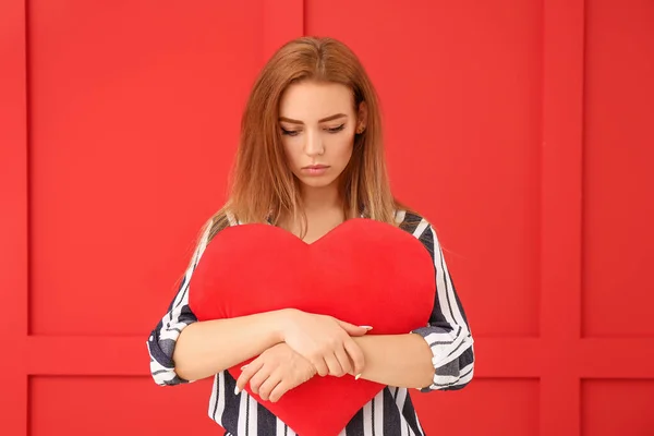 Beautiful sad young woman with big red heart on color background — ストック写真