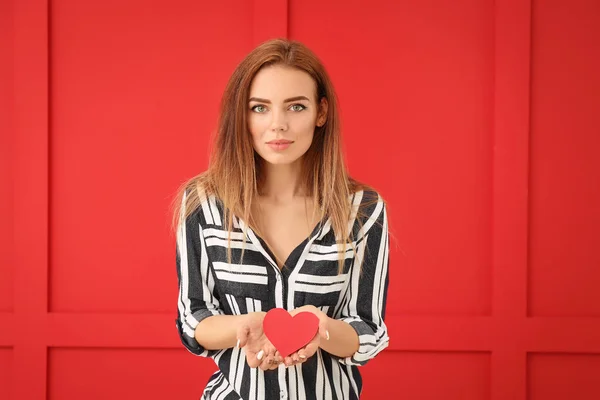 Beautiful young woman with red heart on color background — Stock Photo, Image