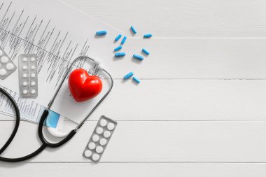 Stetoskop, kardiyogram, kırmızı kalp ve beyaz tahta arka planda haplar. Kardiyoloji kavramı