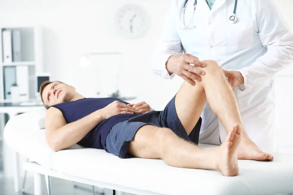 Doctor examining sportsman with joint pain in clinic — Stockfoto