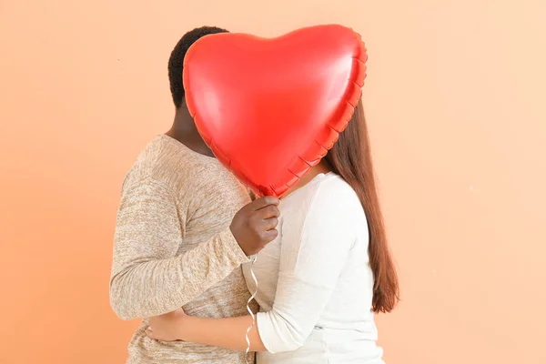 Happy interracial couple with heart-shaped balloon on color background — Stock Photo, Image