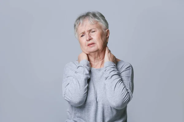 Seniorin leidet unter Nackenschmerzen auf grauem Hintergrund — Stockfoto