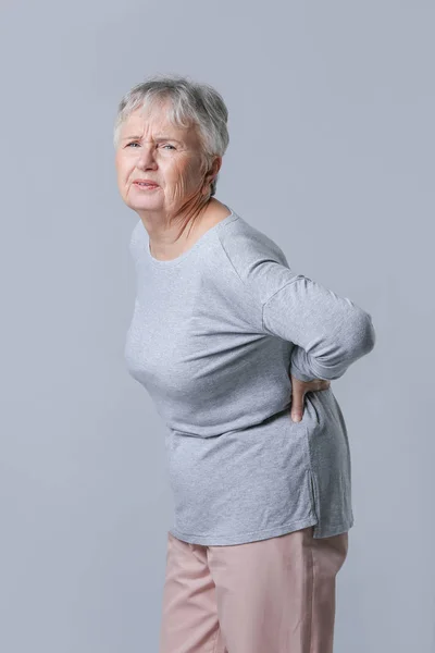 Senior vrouw die lijden aan rugpijn op grijze achtergrond — Stockfoto