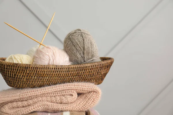 Basket with knitting yarns and clothes on grey background — Stock Photo, Image