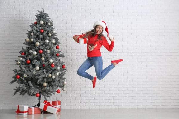 Jumping woman with gifts near Christmas tree indoors — Stock Photo, Image