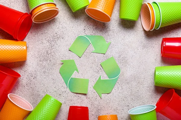 Copos de plástico e símbolo de reciclagem no fundo claro — Fotografia de Stock
