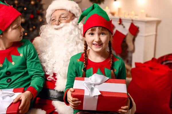 Santa Claus and little elf kids with gifts in room decorated for Christmas — Stock Photo, Image