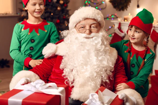 Santa Claus and little elf kids with gifts in room decorated for Christmas — Stock Photo, Image