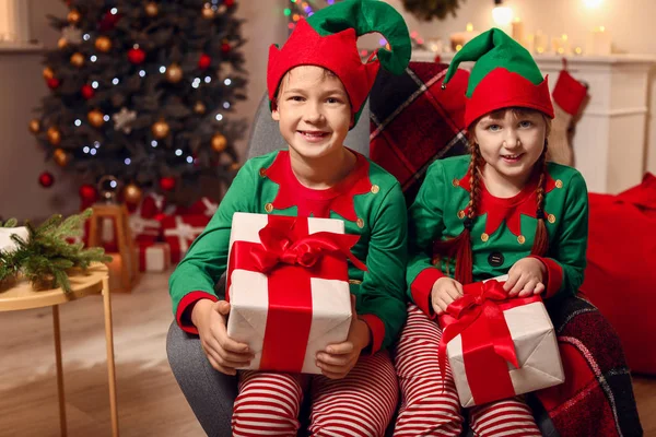 Little children in costume of elf and with gifts in room decorated for Christmas — Stock Photo, Image