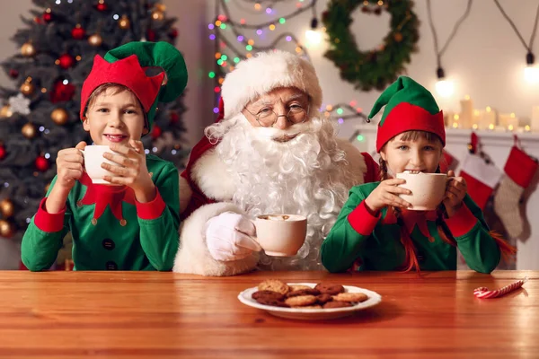 Jultomten och små barn dricker varm choklad med kakor i rummet dekorerade för jul — Stockfoto