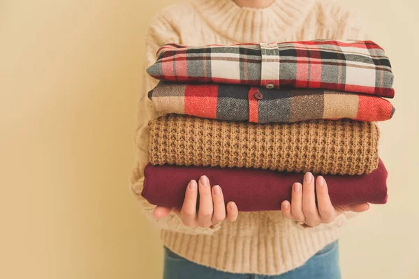 Woman with stack of winter clothes on color background, closeup — Stock Photo, Image
