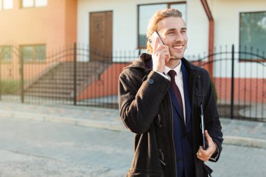 Erkek emlakçı dışarıda cep telefonuyla konuşuyor.