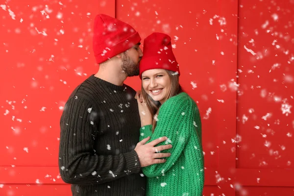 Portrait of happy couple in winter clothes and flying snow on color background — Stock Photo, Image