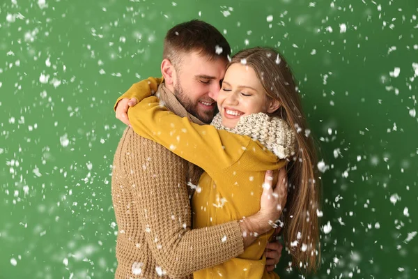 Portrait of happy couple in winter clothes and flying snow on color background — Stock Photo, Image