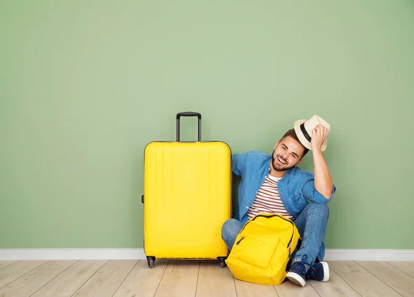 Giovane turista maschio con bagagli seduto vicino alla parete di colore — Foto Stock