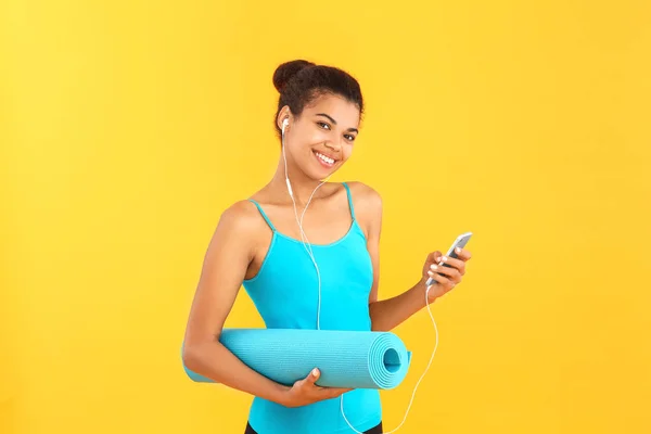 Sporty African-American woman with yoga mat and mobile phone on color background — Stock Photo, Image