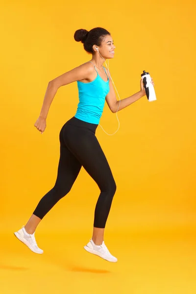 Running African-American woman with bottle of water on color background — Stock Photo, Image