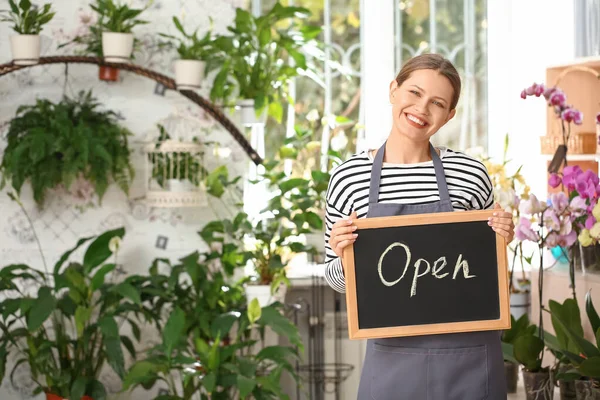 Florist holding chalkboard with text OPEN in shop — Stock Photo, Image