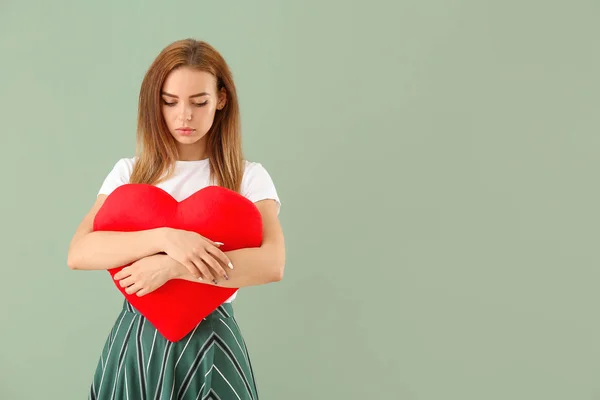 Beautiful sad young woman with big red heart on color background — ストック写真