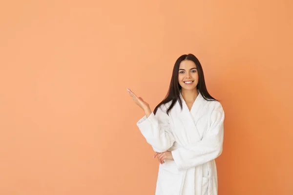 Beautiful young woman in bathrobe on color background — Stock Photo, Image