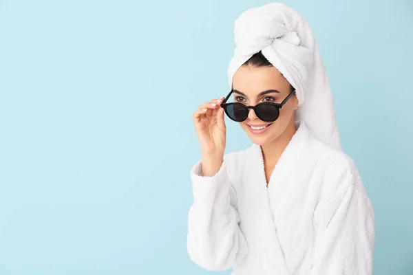 Beautiful young woman in bathrobe and with sunglasses on color background — Stock Photo, Image