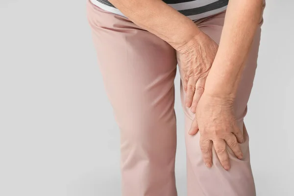 Starsza kobieta cierpiąca na ból kolana na szarym tle, zbliżenie — Zdjęcie stockowe