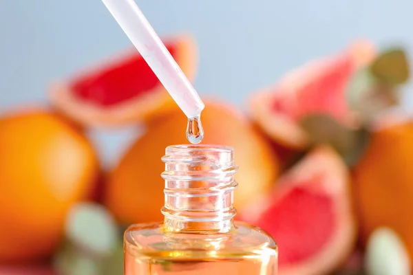 Grapefruit oil dripping into bottle on blurred background, closeup