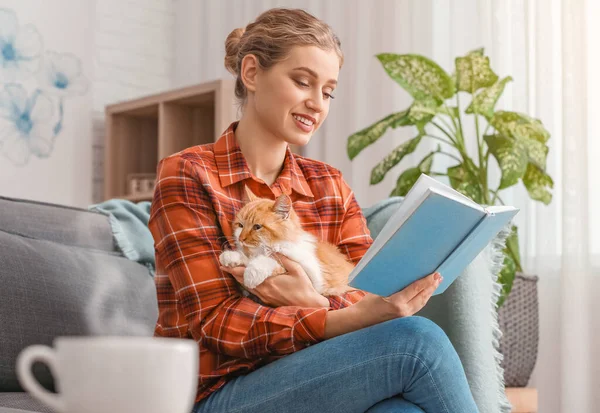 Beautiful young woman with cute cat reading book at home — Stock Photo, Image