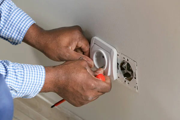 African-American electrician replacing socket in room, closeup