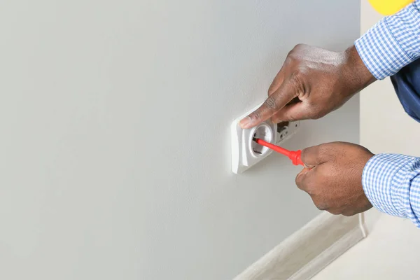 African-American electrician replacing socket in room