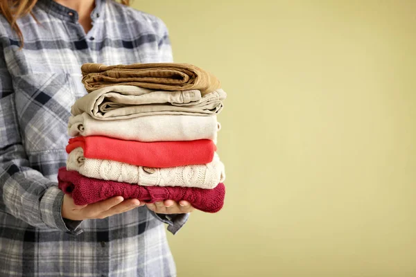 Woman with stack of warm clothes on color background — Stockfoto