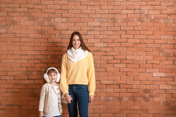 Милая маленькая девочка с мамой в зимней одежде возле кирпичной стены — стоковое фото