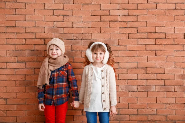 Lindos niños pequeños en ropa de invierno cerca de la pared de ladrillo —  Fotos de Stock