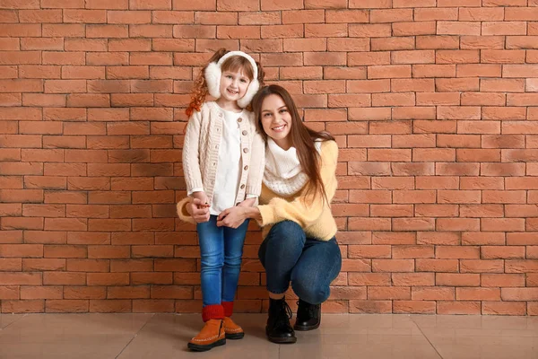Tuğla duvarın yanında annesi kışlık giysiler içinde tatlı küçük bir kız. — Stok fotoğraf