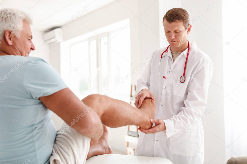 Doctor examining mature man with joint pain in clinic