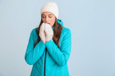 Kışın giyinmiş genç bir kadın. Renkli arka planda nefesiyle elleri ısıtıyor.