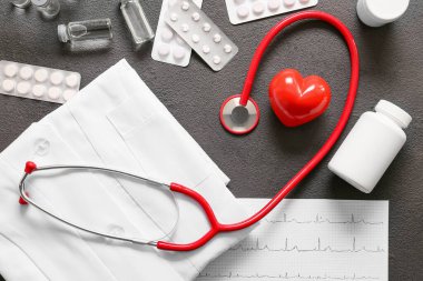 Stetoskop, doktor üniforması, kardiyogram, kalp ve haplar gri arka planda. Kardiyoloji kavramı