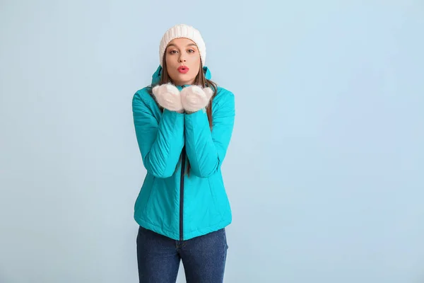 Happy young woman in winter clothes sending kiss on color background — Stock Photo, Image