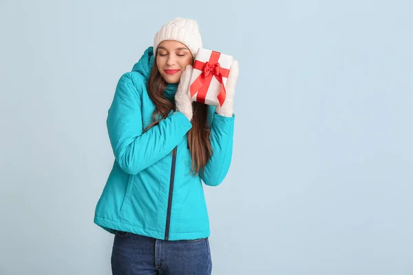 Glückliche junge Frau in Winterkleidung und mit Weihnachtsgeschenk auf farbigem Hintergrund — Stockfoto