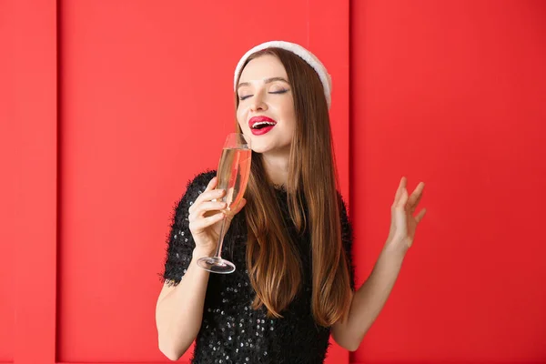 Beautiful young woman in Santa hat and with champagne near color wall — Stock Photo, Image