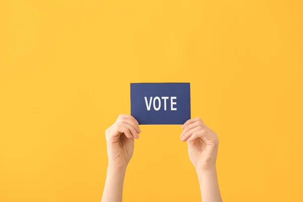 Mãos segurando papel com texto VOTE no fundo da cor — Fotografia de Stock
