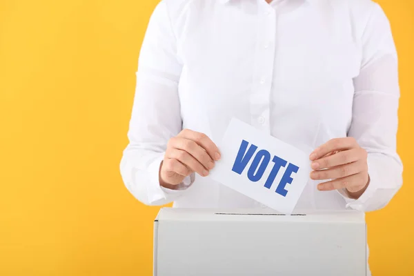 Голосование женщины возле урны для голосования на цветном фоне — стоковое фото