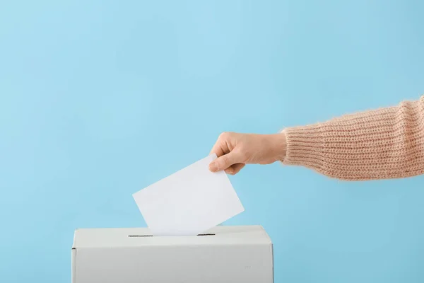 Голосование женщины возле урны для голосования на цветном фоне — стоковое фото