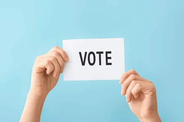 Mãos segurando papel com texto VOTE no fundo da cor — Fotografia de Stock