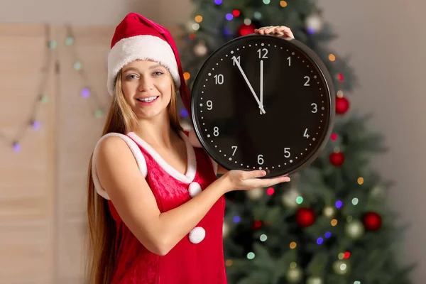 Νεαρή γυναίκα με στολή Αϊ Βασίλη και με ρολόι στο δωμάτιο. Χριστούγεννα αντίστροφη μέτρηση έννοια — Φωτογραφία Αρχείου