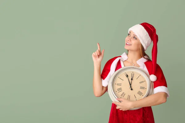 Νεαρή γυναίκα με κοστούμι Σάντα και με το ρολόι να δείχνει κάτι στο φόντο χρώμα. Χριστούγεννα αντίστροφη μέτρηση έννοια — Φωτογραφία Αρχείου